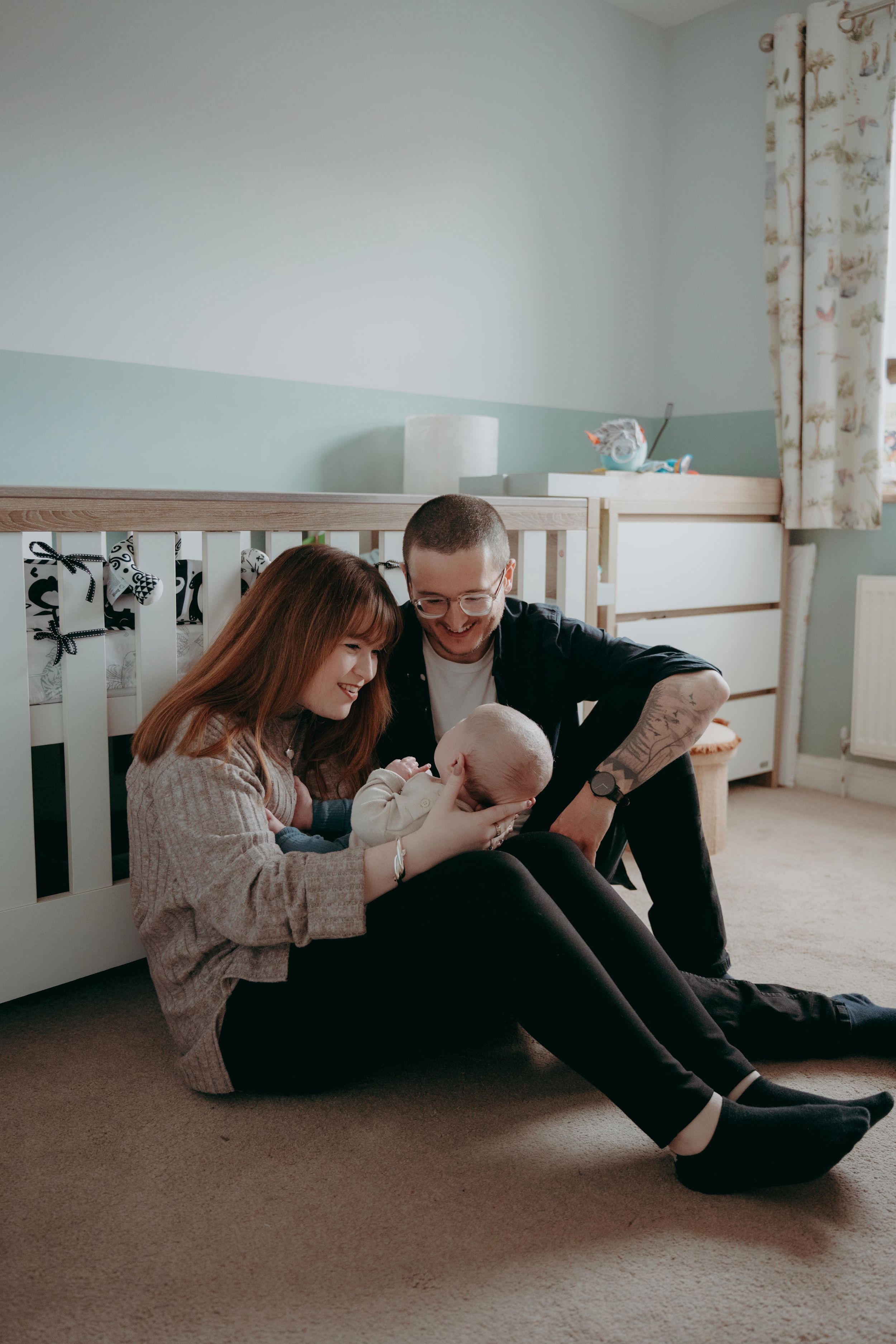 A family sits together on the floor of a nursery room sharing a tender moment with their baby.