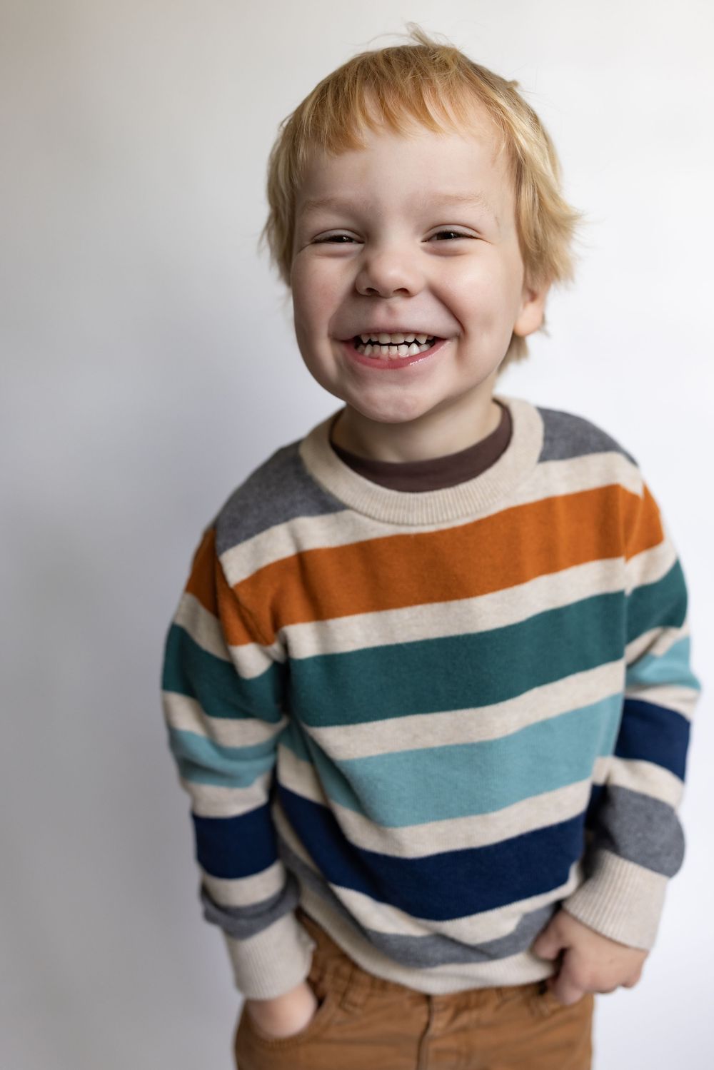 Close-up of a cheerful young boy smiling broadly in a colorful striped sweater with hands behind back.