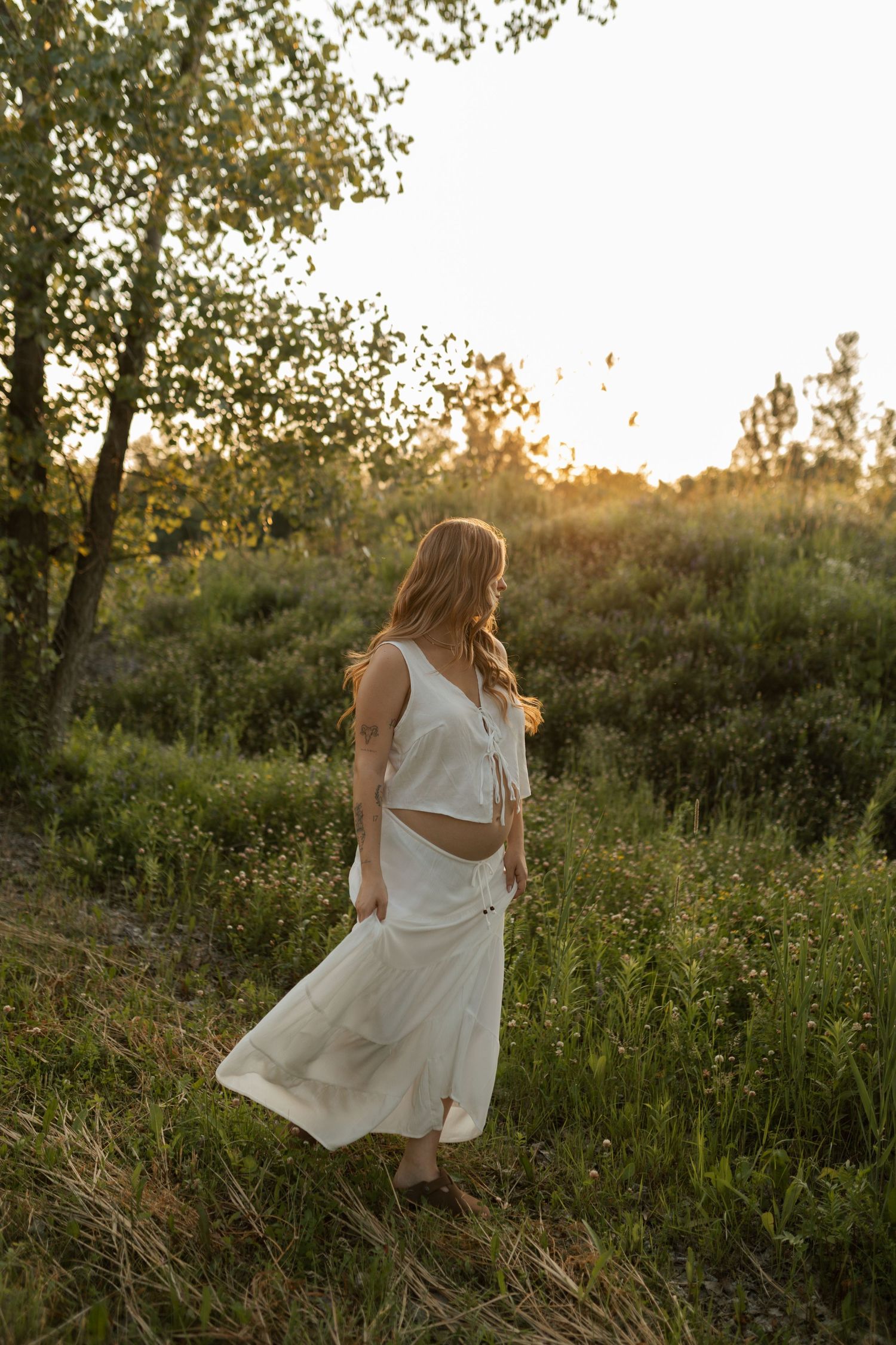A bride and groom embrace in a lush green meadow with a forested hillside backdrop on their wedding day.