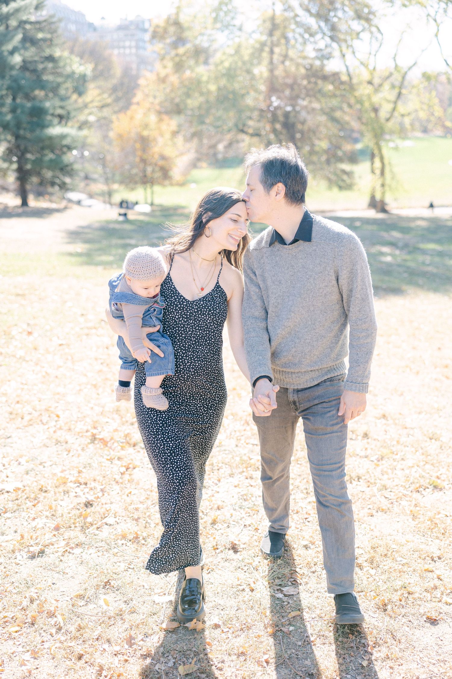 Three people taking a romantic autumn stroll through a park filled with golden fallen leaves on a sunny day.