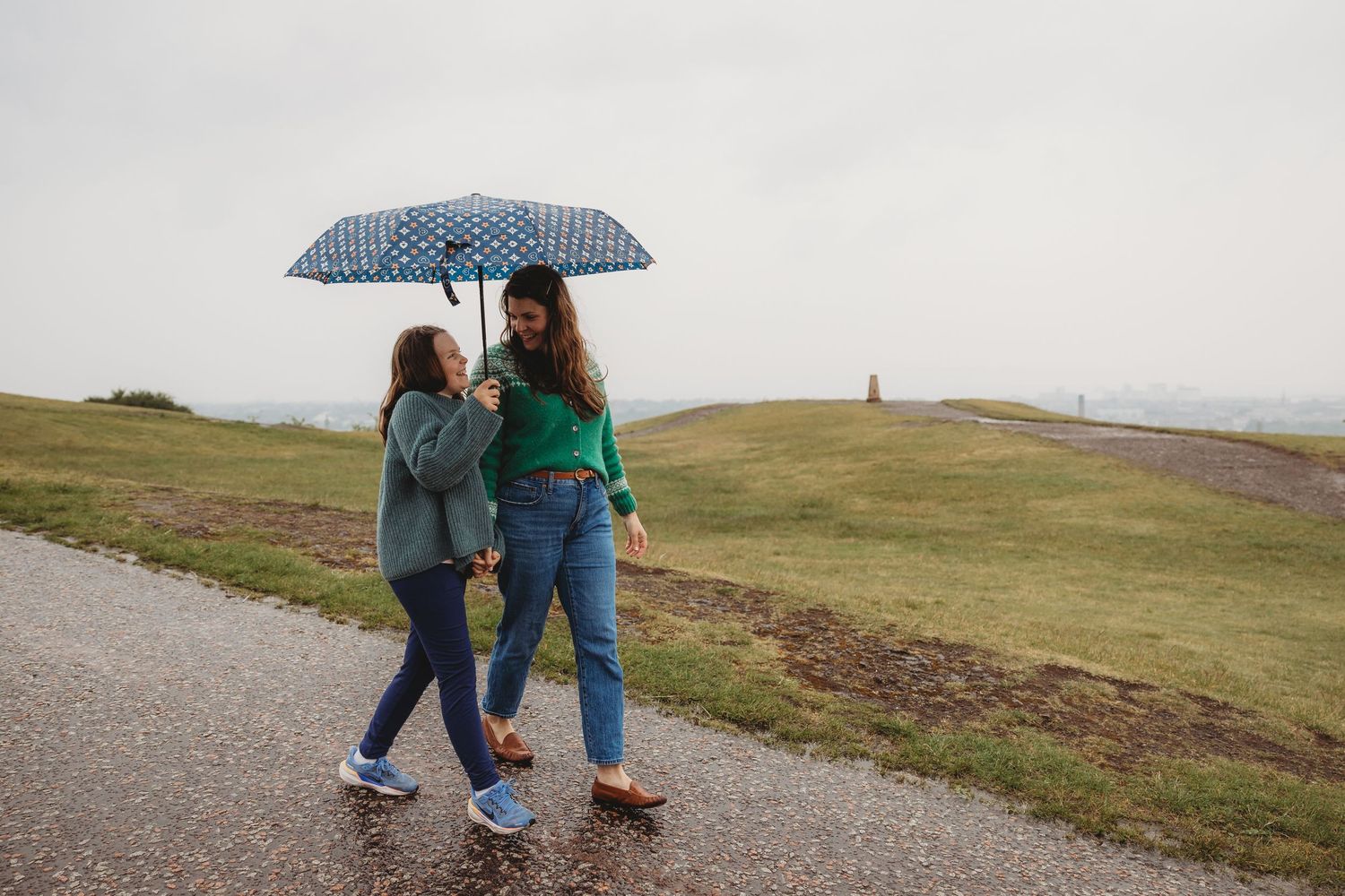Two people walking with umbrellas along a misty coastal path on a rainy day in Ireland.