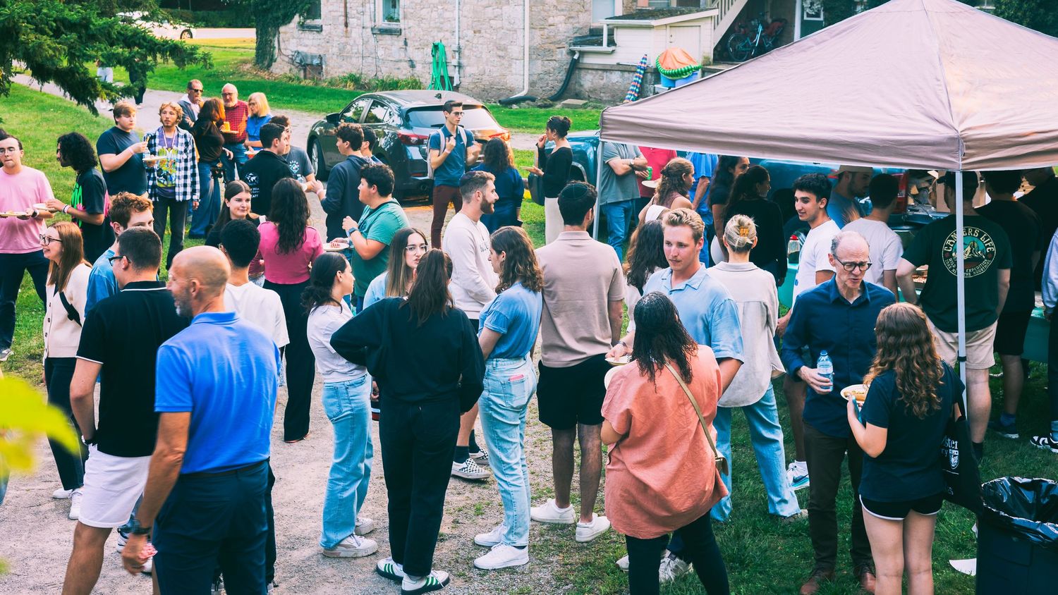 A crowd of people gather at an outdoor event with tents and vendors on a sunny day.