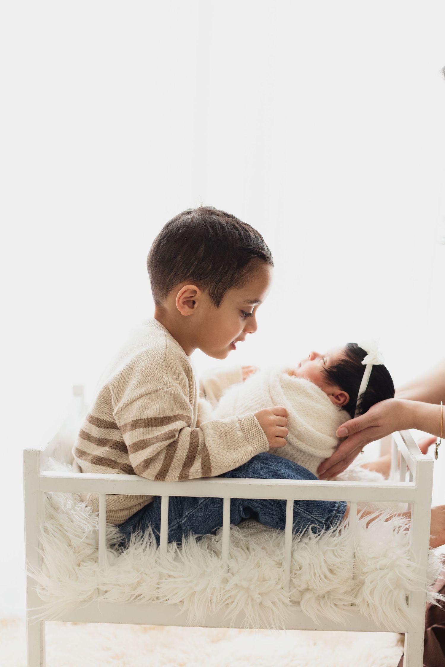 Two children share a tender moment while playing on a white wooden bed with fluffy white bedding. Elizabeth Lang Photography Surrey