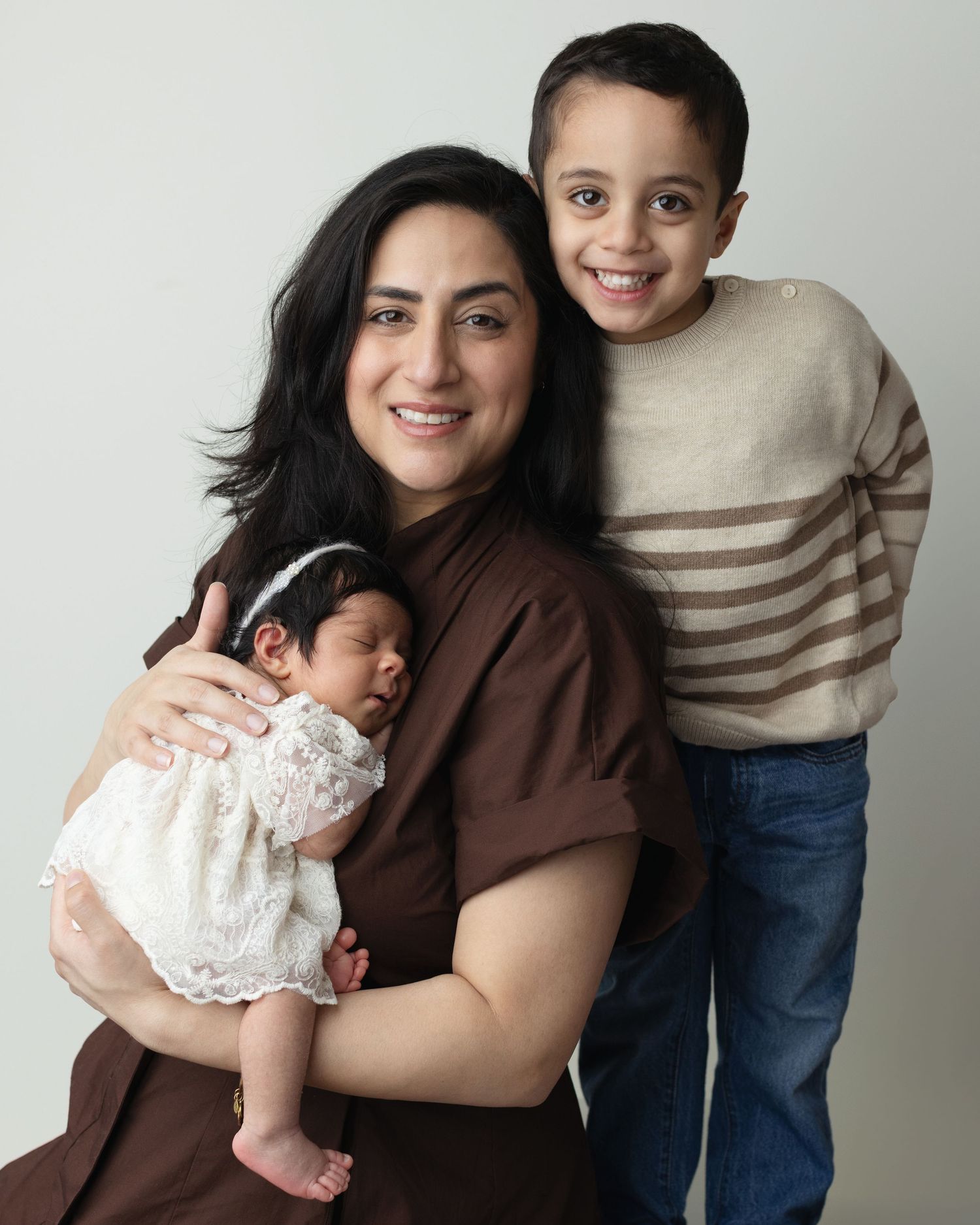 A family portrait series showing tender moments with a baby in white lace dress against a light background. Elizabeth Lang Photography Surre