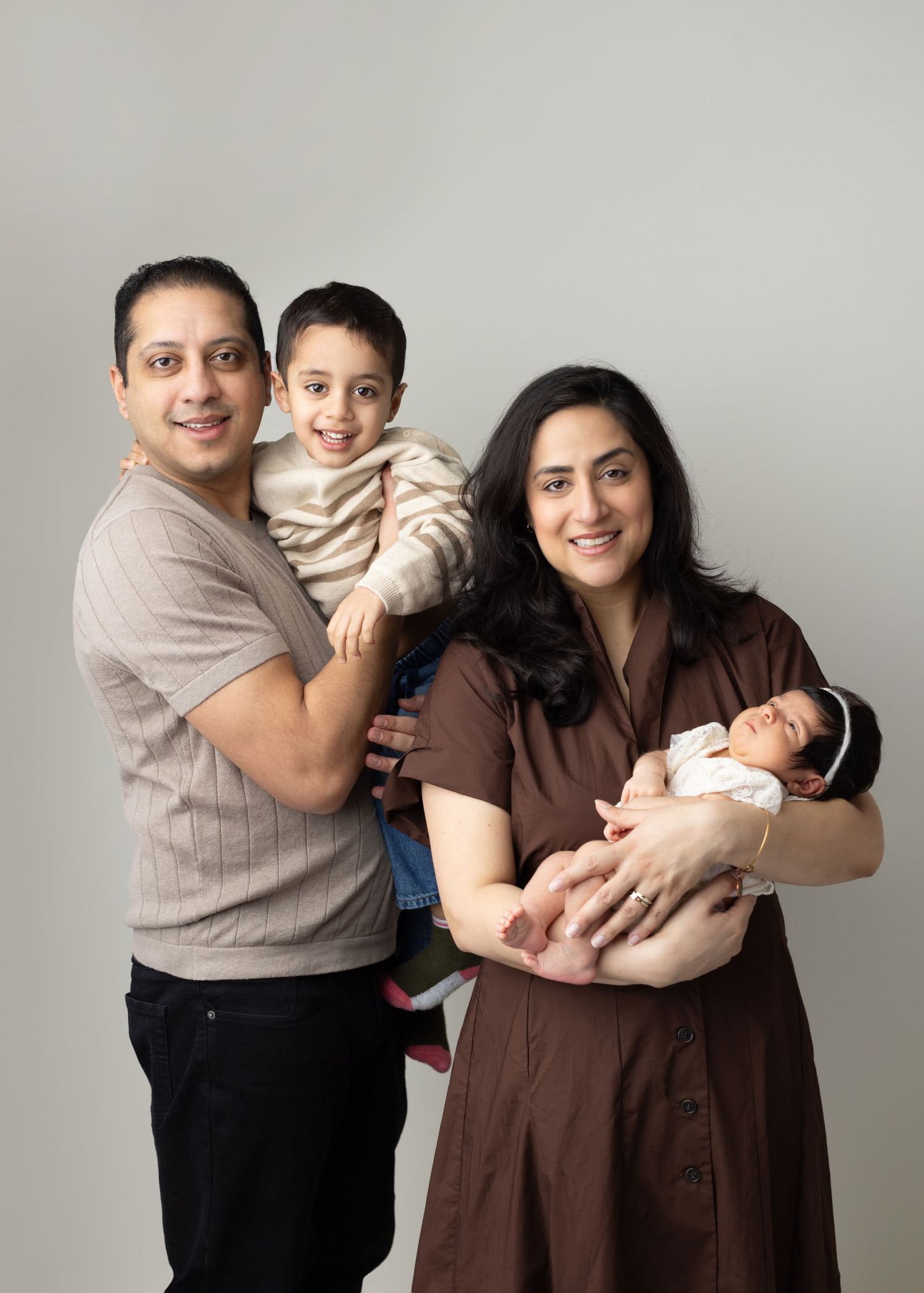 A family of four poses together against a neutral background in coordinated brown and beige outfits. Elizabeth Lang Photography Surrey