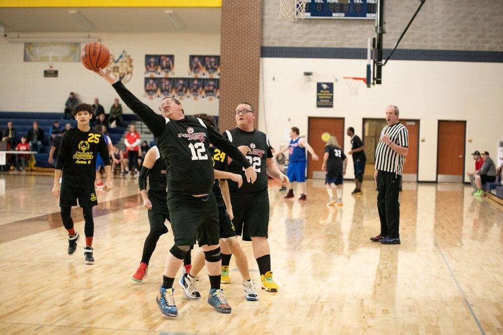 Players compete in an intense basketball game on a wooden court in a gymnasium.
