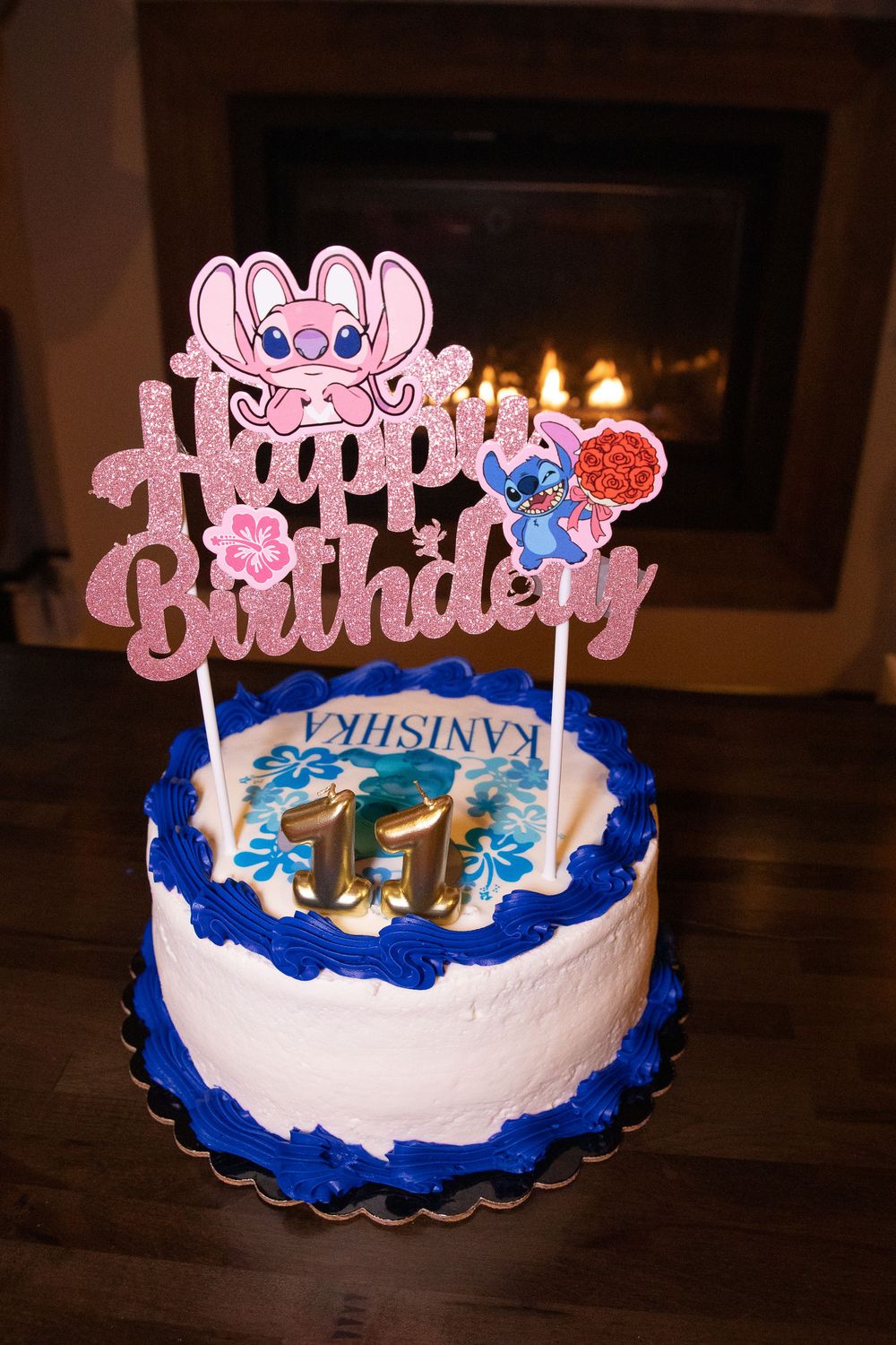 A white and blue birthday cake with pink 'Happy Birthday' topper shown from different angles on a dark wooden table.