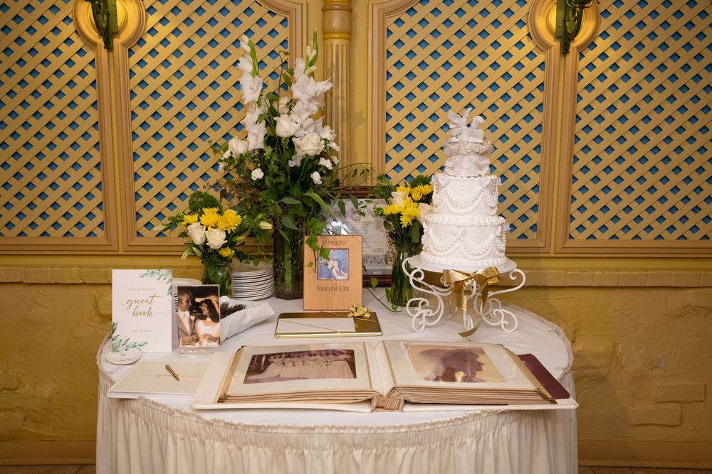 Wedding dessert table with white tiered cake, cupcakes, and yellow floral decorations against a latticed wall.