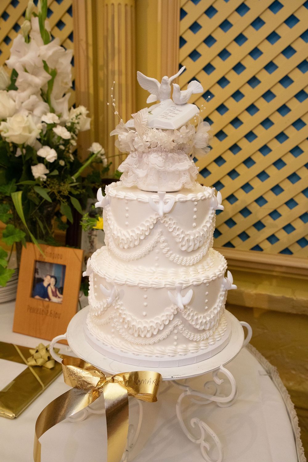 Elegant white wedding cake decorated with delicate lace patterns, pearls, and doves displayed on a silver cake stand.