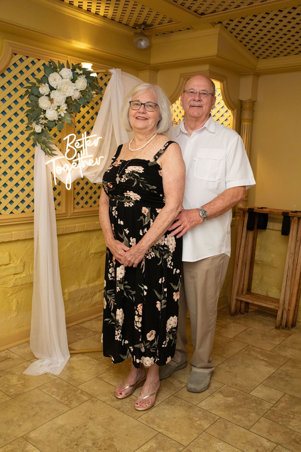 A couple dances together in a reception hall with white lattice decor and floral arrangements.