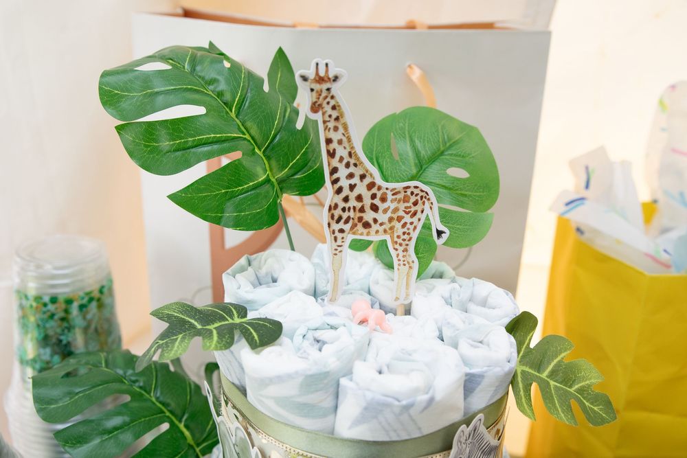Tropical monstera leaves and white baby diapers arranged in a modern diaper cake display with giraffe decorations.