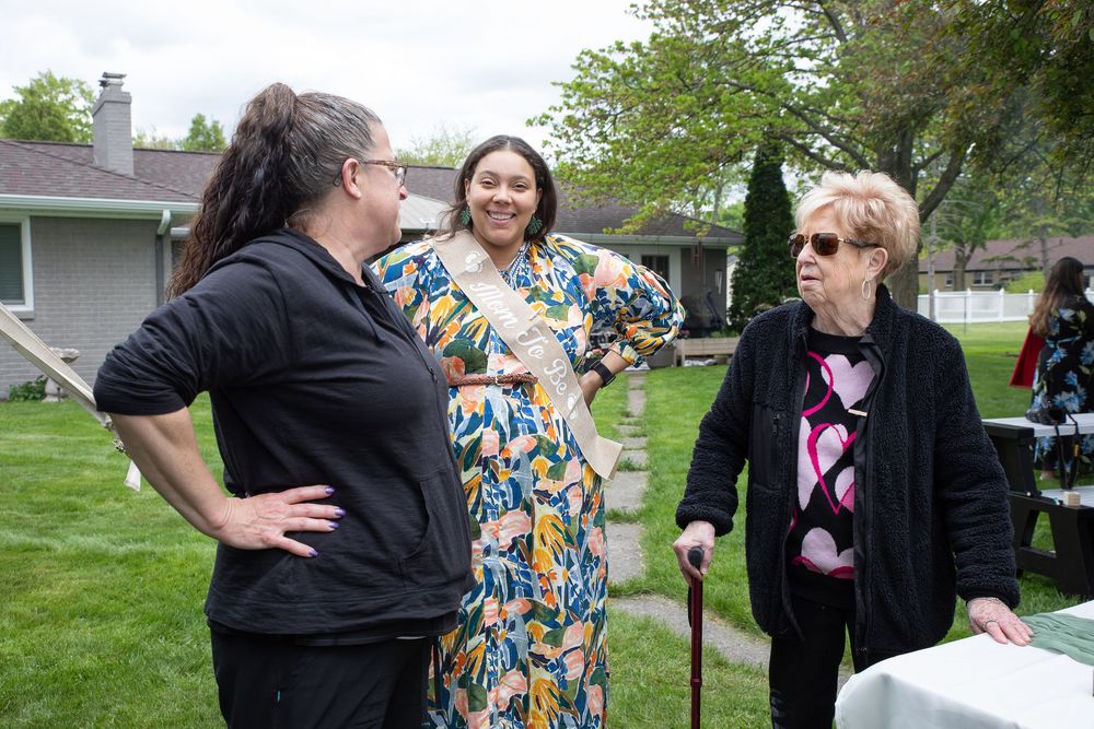 A group of people gather outdoors for a social event in a backyard garden setting.