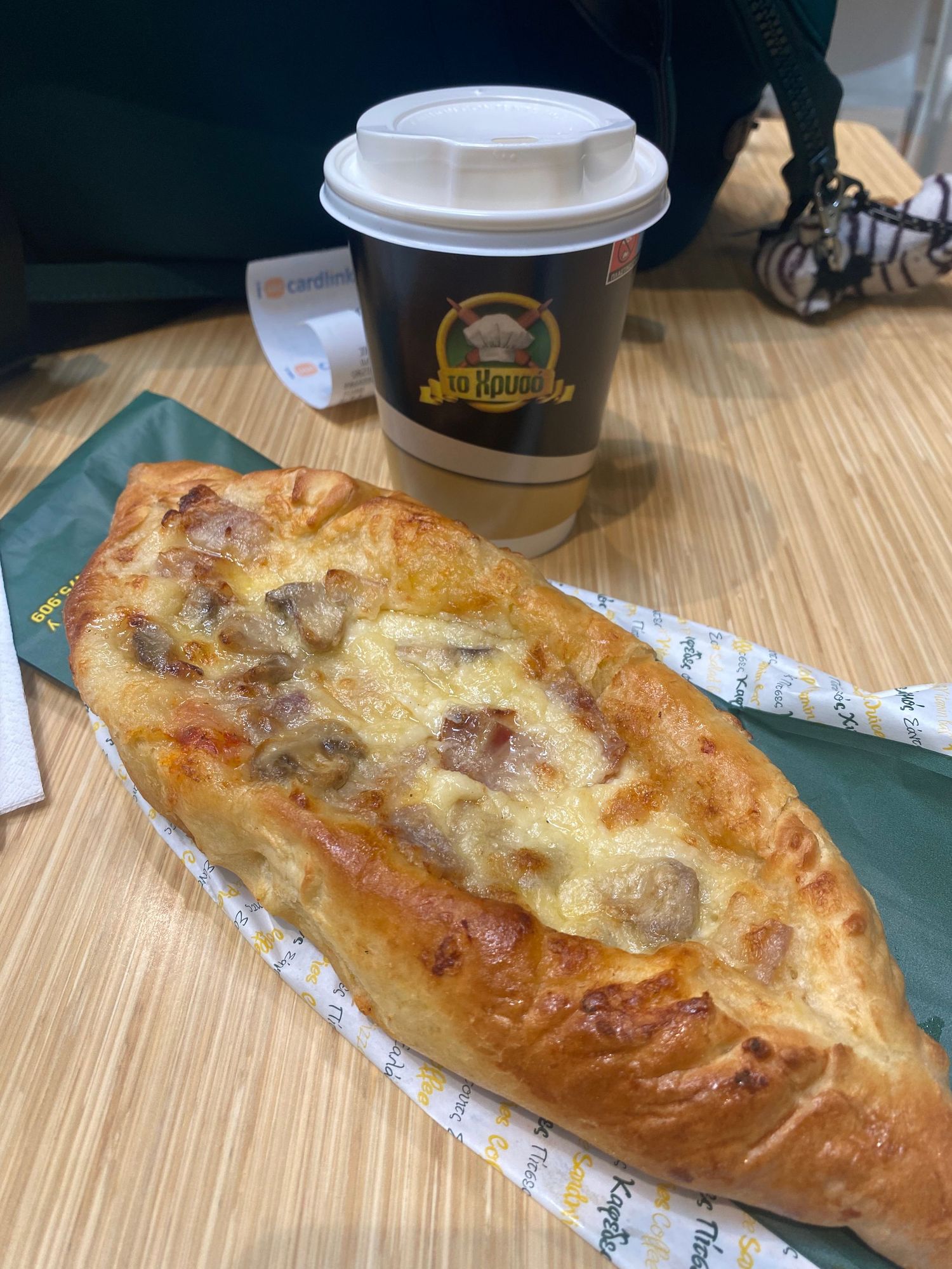 A freshly baked calzone with golden brown crust and melted cheese filling sits on a wooden table next to coffee cups.