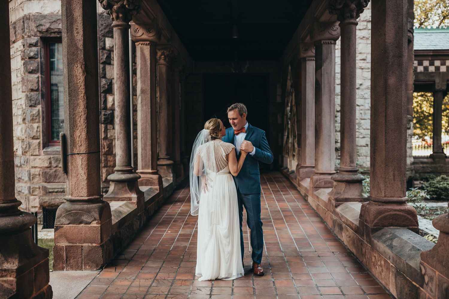 A couple shares an intimate moment in a historic stone archway corridor with warm lighting and architectural details.