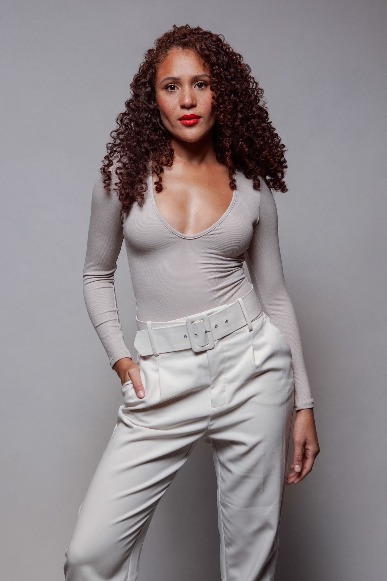 A model poses in a black crop top and white blazer against a beige background in a fashion photo series.