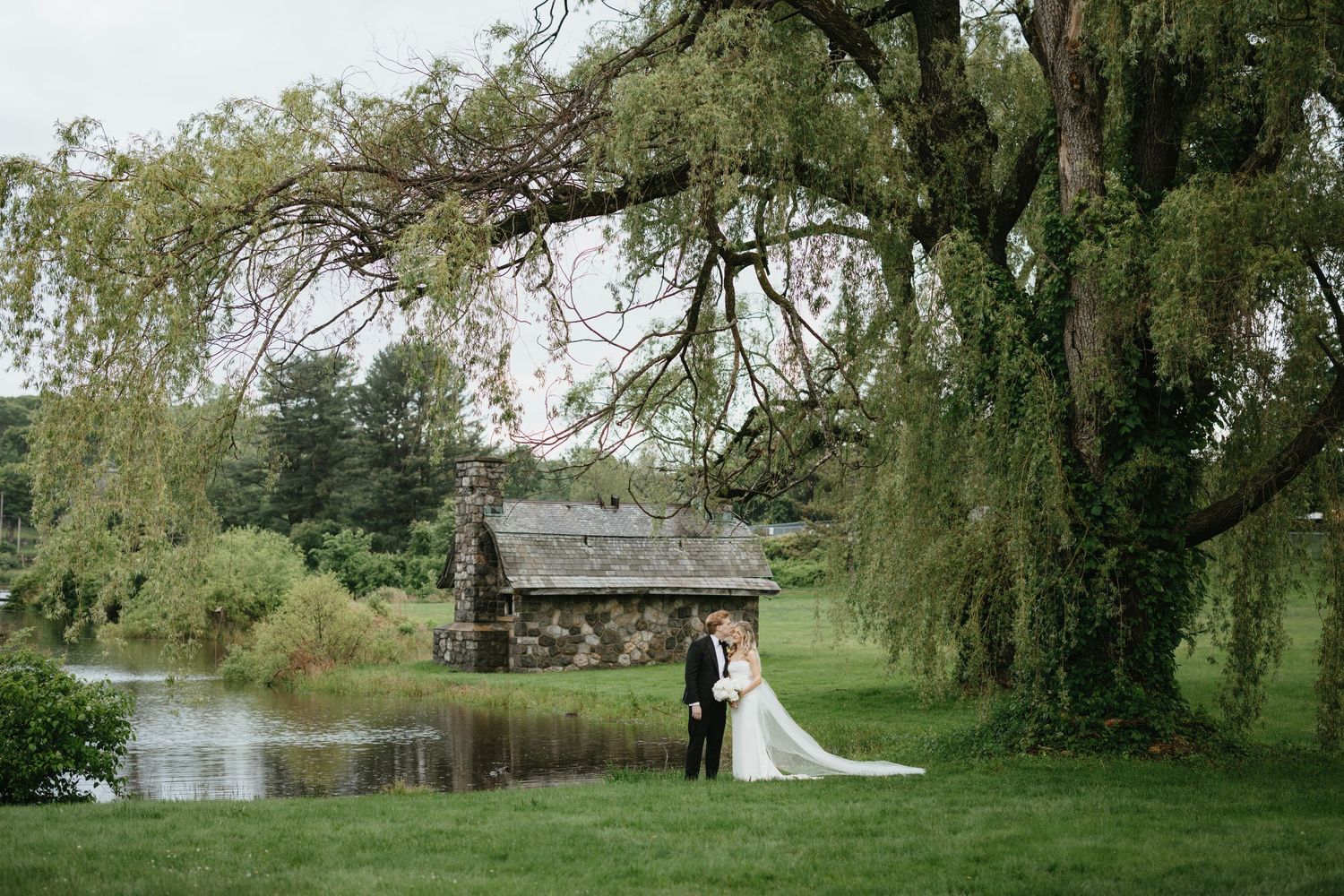 A rustic driftwood wedding arch stands on a stone path overlooking mountain views under cloudy skies.