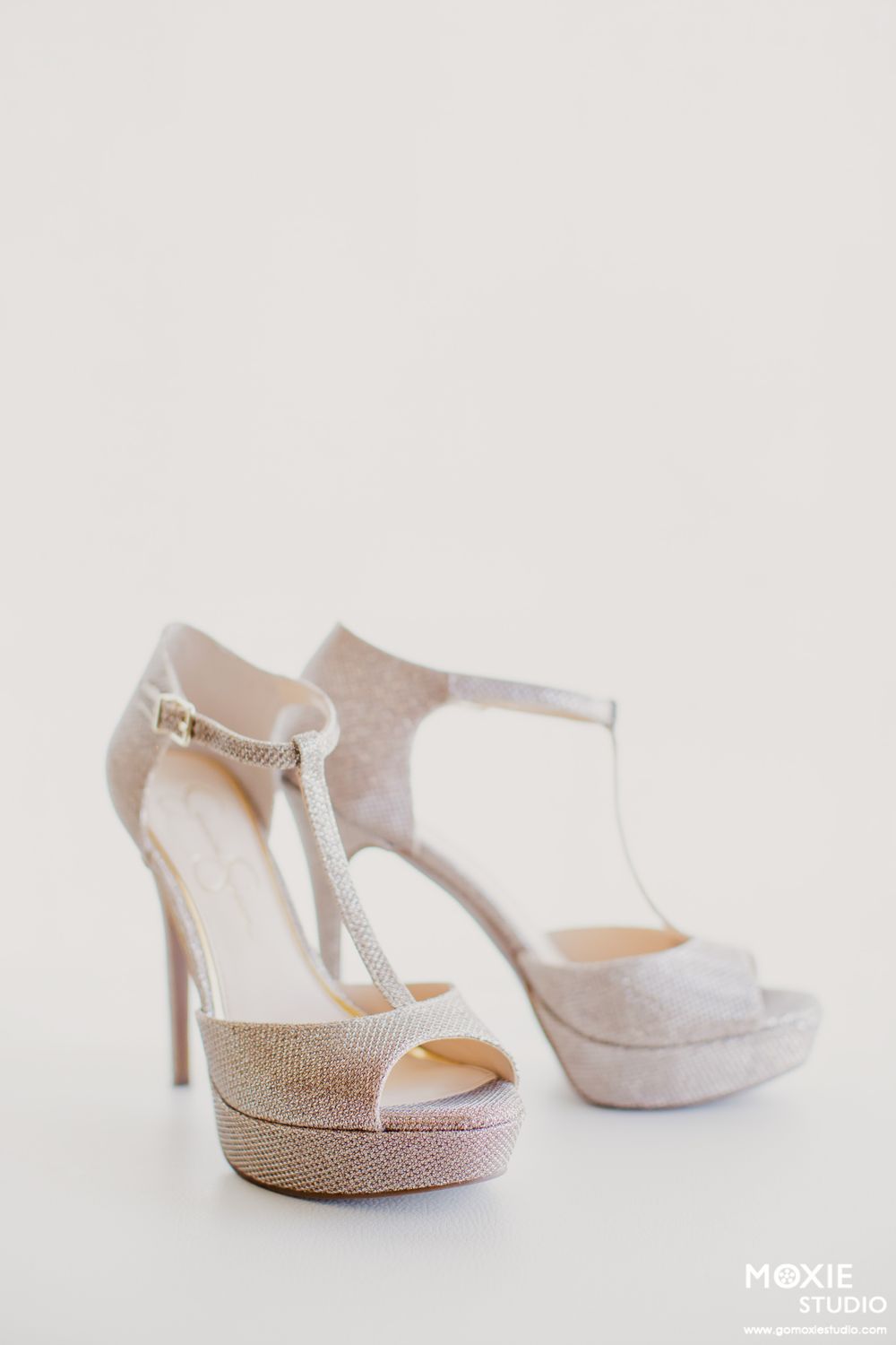Elegant white satin bridal heels with sparkly rhinestone details and ankle straps displayed from different angles.