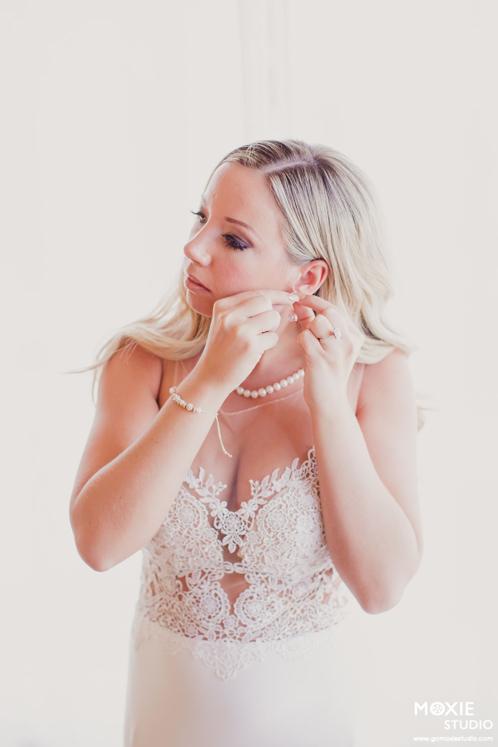 A bride in a white lace gown puts on pearl earrings in a series of elegant getting-ready photos.