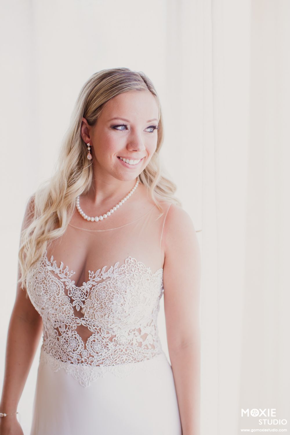 Close-up details of delicate white lace wedding dress bodice with sheer neckline and pearl accents.