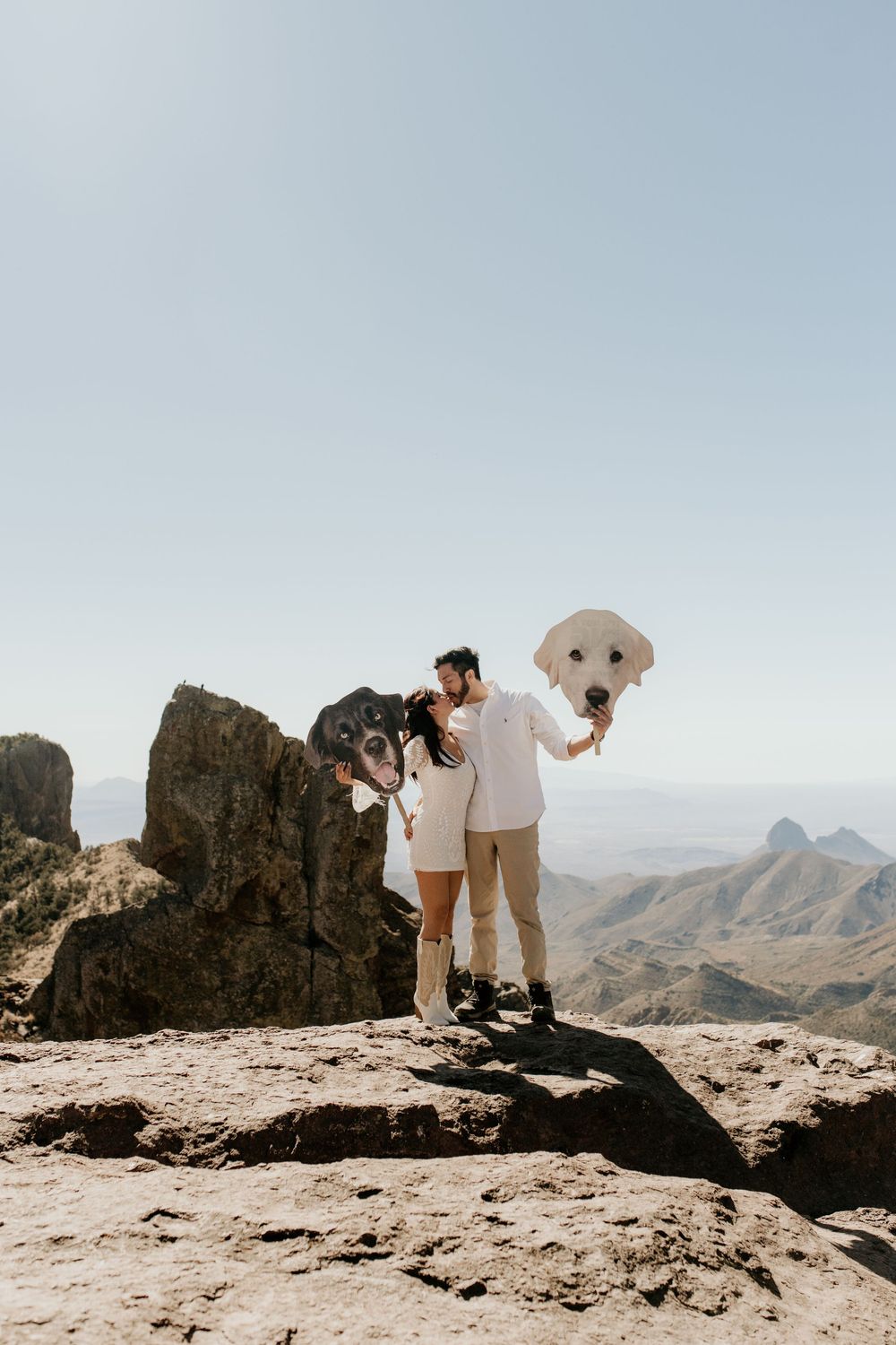 Couple holding giant balloon letters on mountain summit with vast desert views.