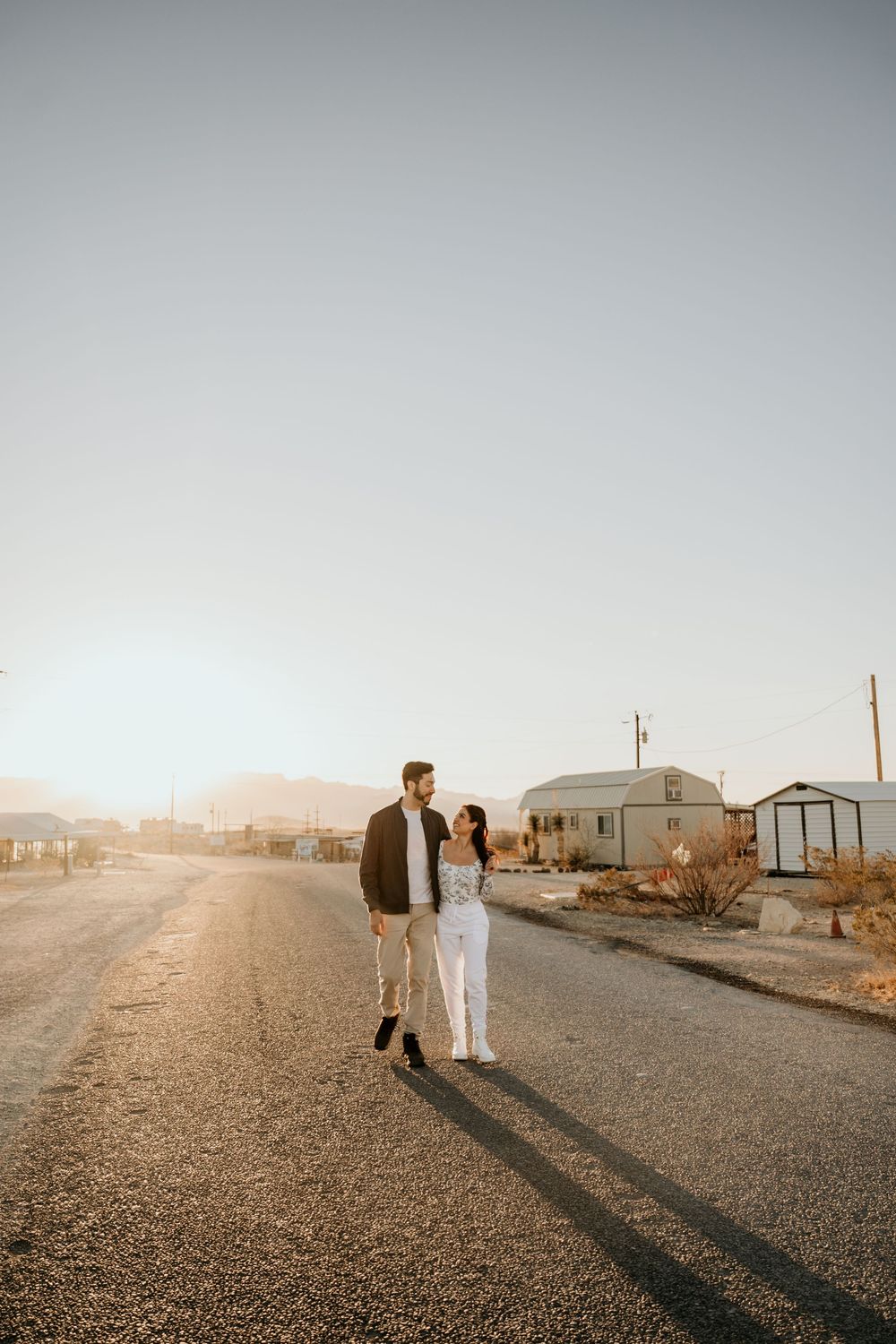 Couple strolling down a gravel road with long shadows in desert setting.
