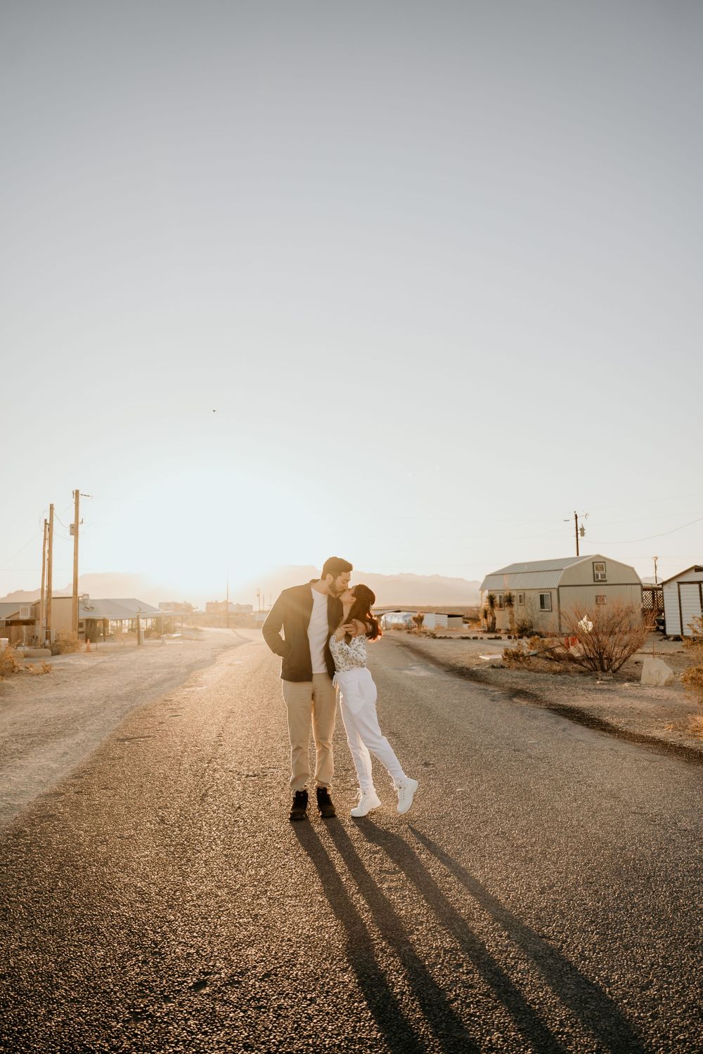 Romantic couple embracing on desert road during golden hour with dramatic shadows.