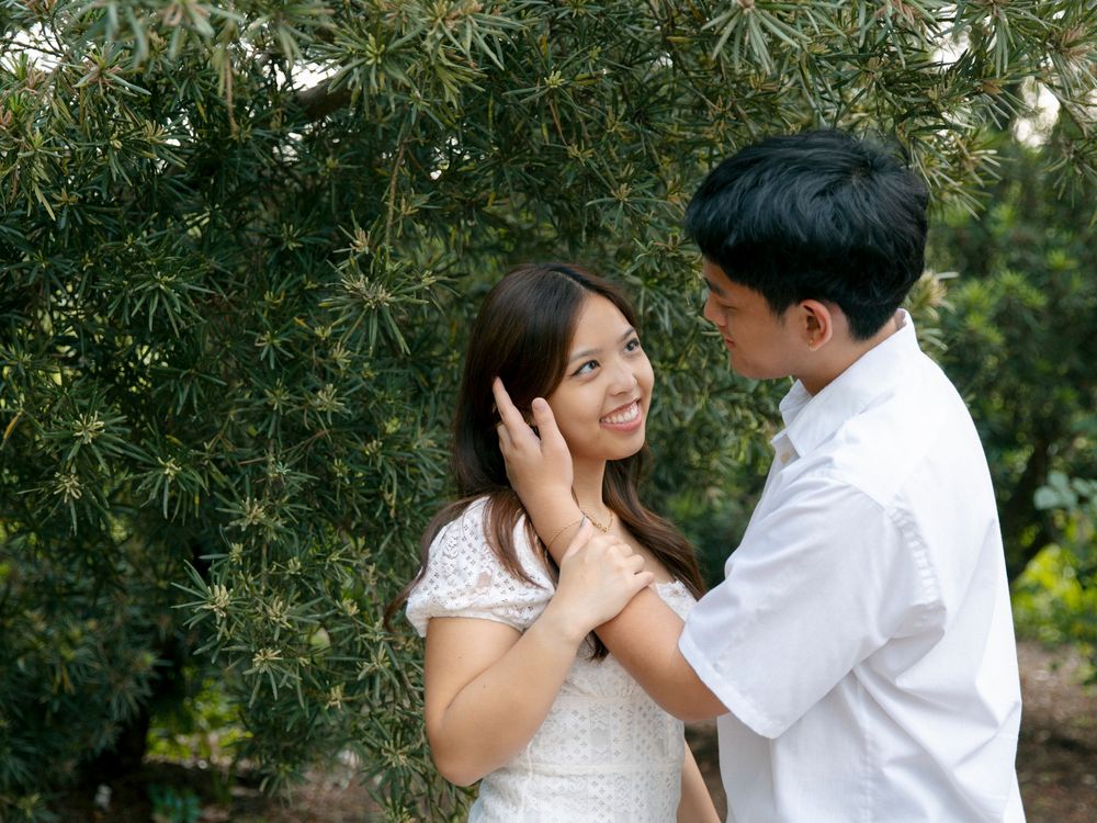 A romantic couple in white attire shares tender moments under olive trees in an outdoor garden setting.