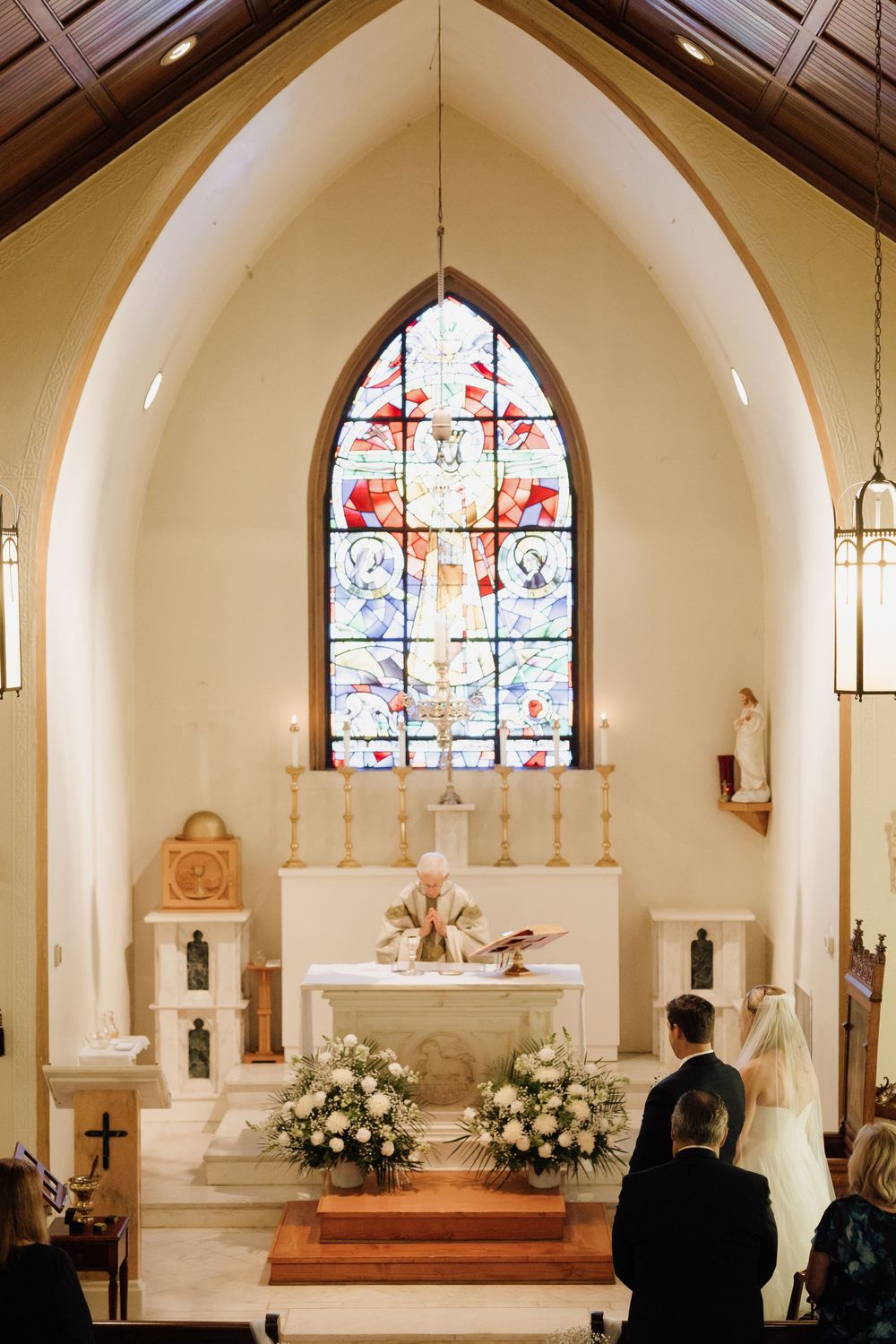 Interior of a church sanctuary with stained glass windows, white arched ceilings, and floral arrangements at the altar.