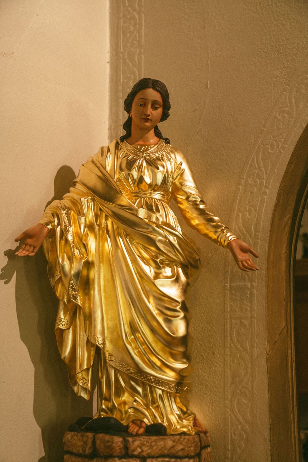 A series of golden metallic sculptures mounted on a wall showing flowing robes in dramatic poses.