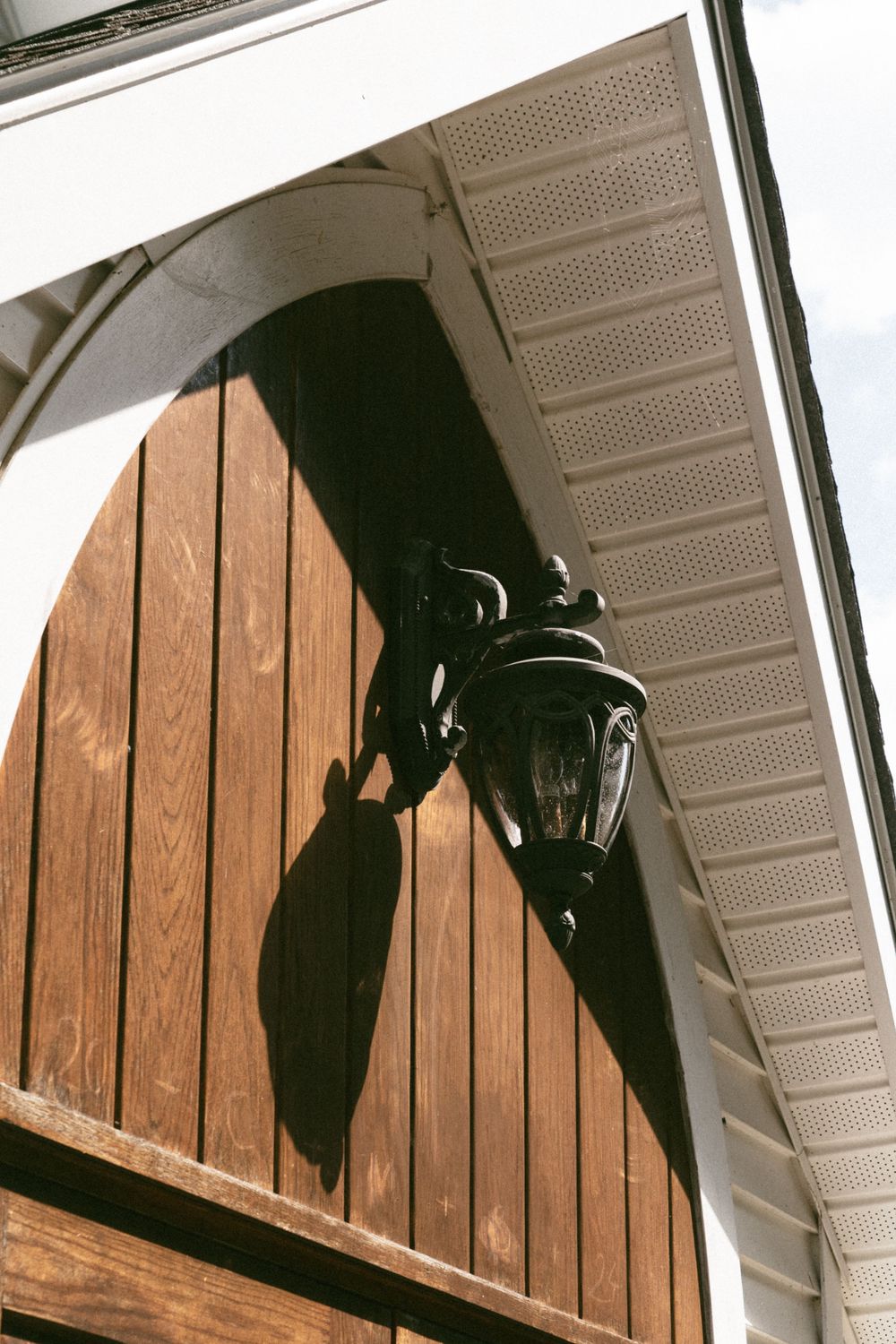 Silhouette of a cat climbing on wooden panels under white eaves against a bright sky.