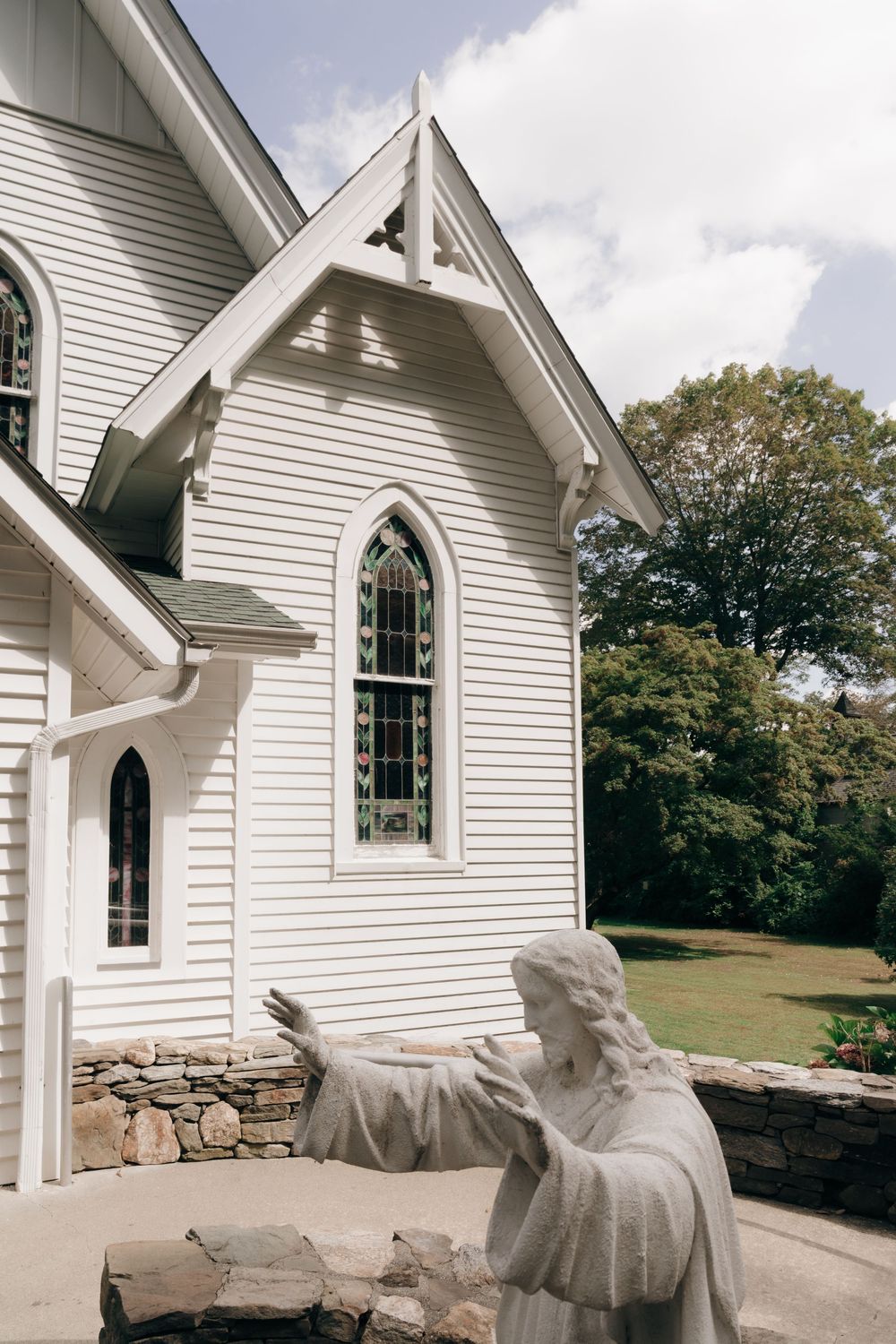 Traditional white wooden church exterior with Gothic arched windows and stone foundation.