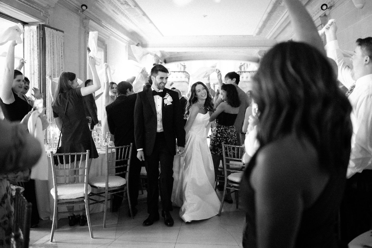 Black and white photo of a wedding celebration with guests gathered in an elegant indoor reception venue.