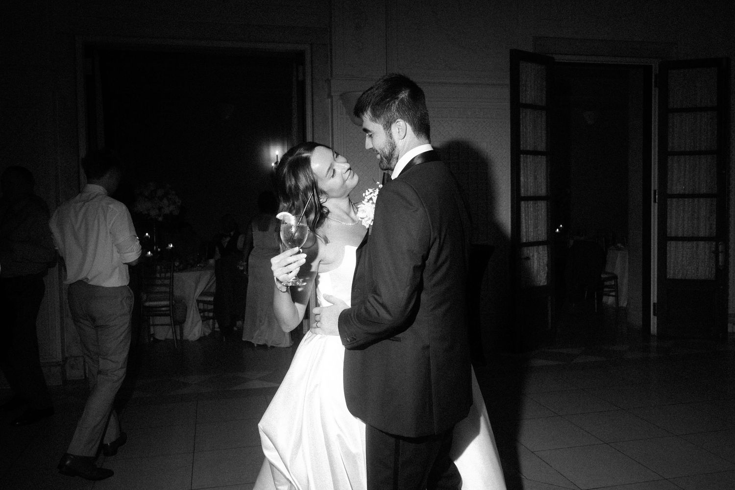 A romantic couple dancing in a dimly lit ballroom setting during what appears to be a wedding celebration.