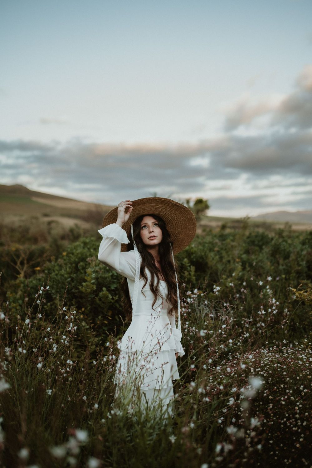 Bride wearing a large sun hat standing in a field of pink and white flowers at De Uijlenes wedding venue