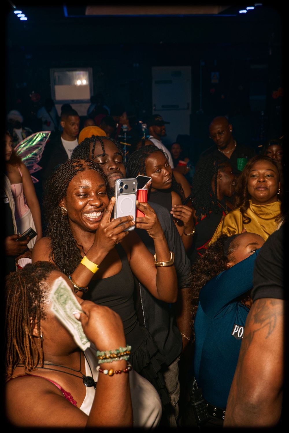 People enjoying themselves at a lively nightclub party while taking photos and dancing in a dark atmosphere.