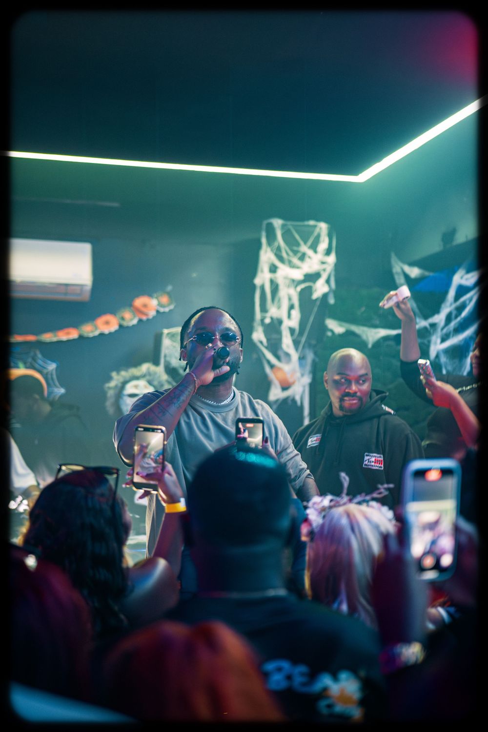 Concert crowd recording performers on stage with phones in a dark venue with blue lighting effects.