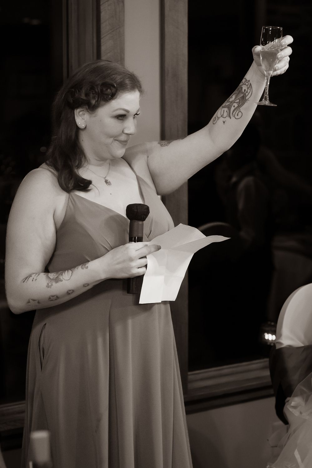 A woman in a sleeveless dress gives an emotional speech at an indoor event while holding a piece of paper.