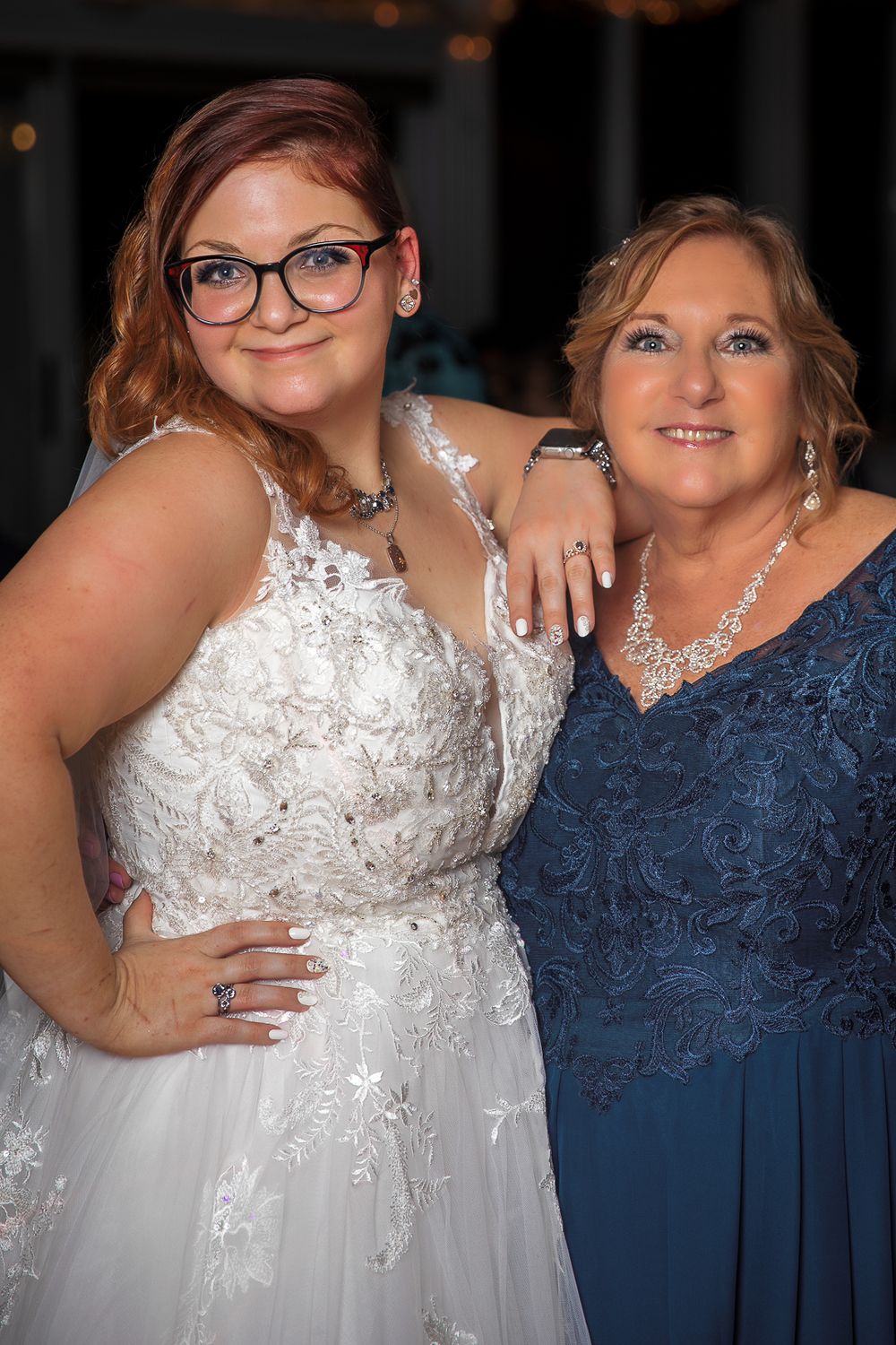 Wedding party members posing together in navy blue and white lace formal dresses with sparkling accessories.