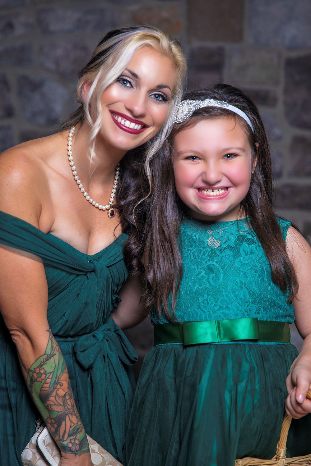 Two people wearing elegant formal dresses in emerald green and turquoise pose together at a special event.