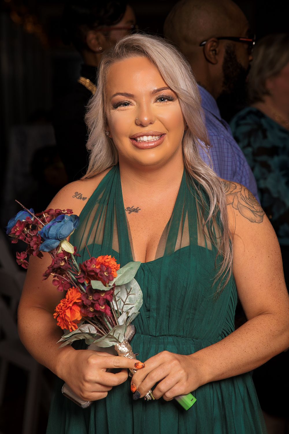 A bridesmaid in an emerald green dress holds a colorful autumn bouquet while smiling.