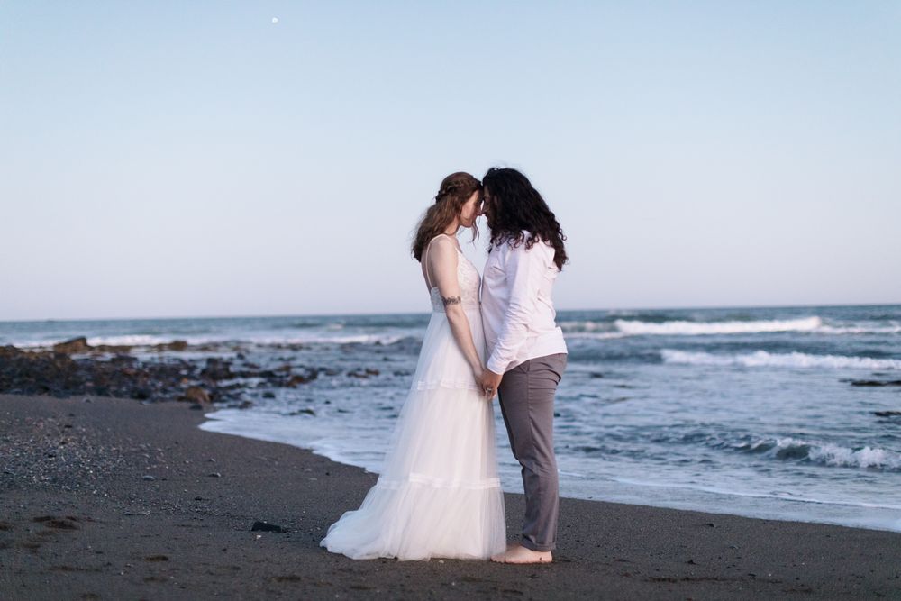 Profile view of husband and wife standing in wedding attire on dark sand beach in Rye, Seacoast New Hampshire. Hampton wedding photographer.