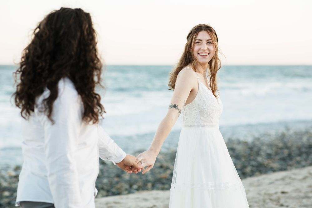 A bride looks back at her husband smiling at golden hour at North Hampton Beach, New Hampshire. North Shore Cohasset wedding photographer.