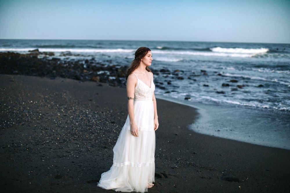 Woman in wedding dress stands on a dark beach in Rye, New Hampshire at blue hour gazing out at ocean. Southern Maine wedding photographer.