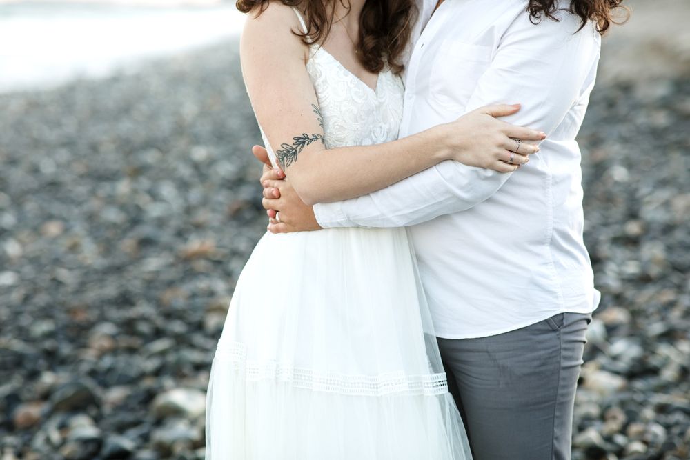 A close up view of husband embracing wife with a tattoo on her arm at a North Hampton Beach in NH. North Shore wedding photographer.