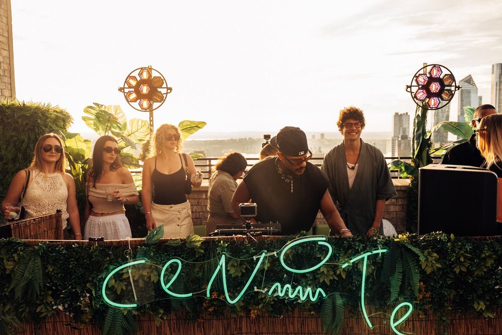 People enjoying an outdoor music festival with neon green signage and lighting at sunset.