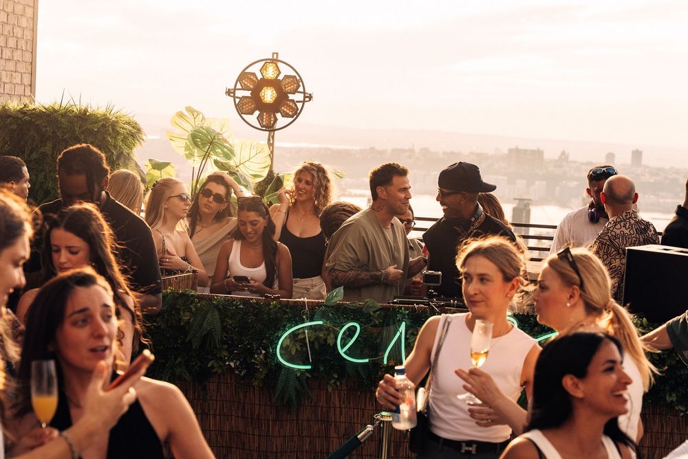 People enjoying drinks and conversation at a rooftop bar with city views during sunset.