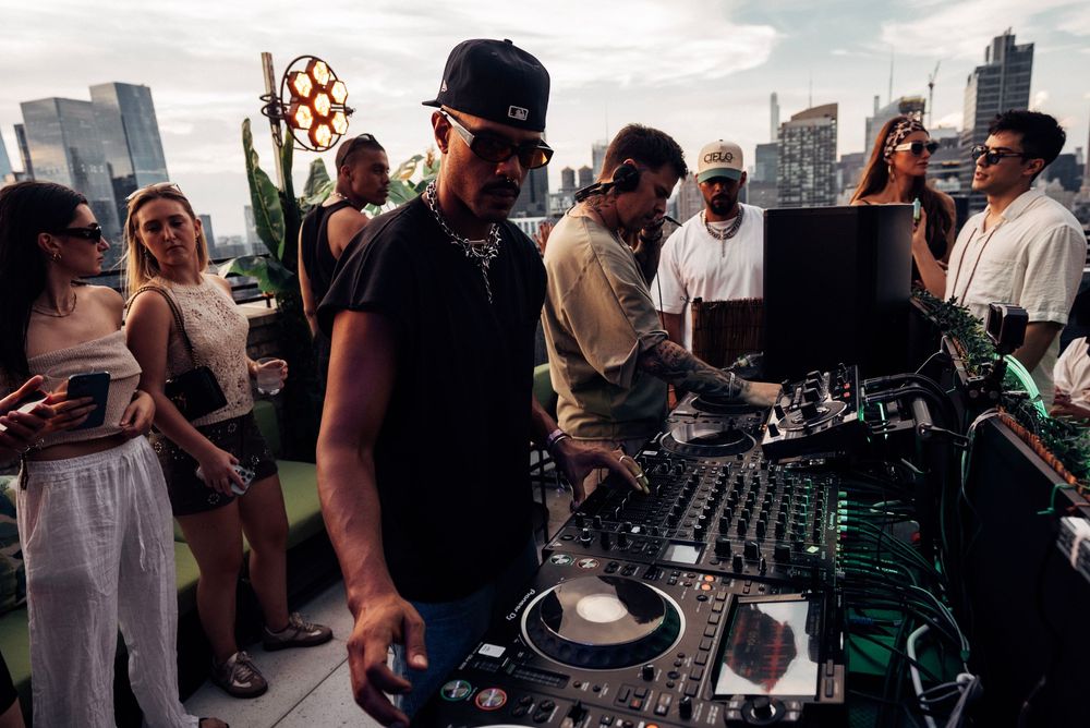 DJ performs at an outdoor rooftop event with city buildings visible in the background.