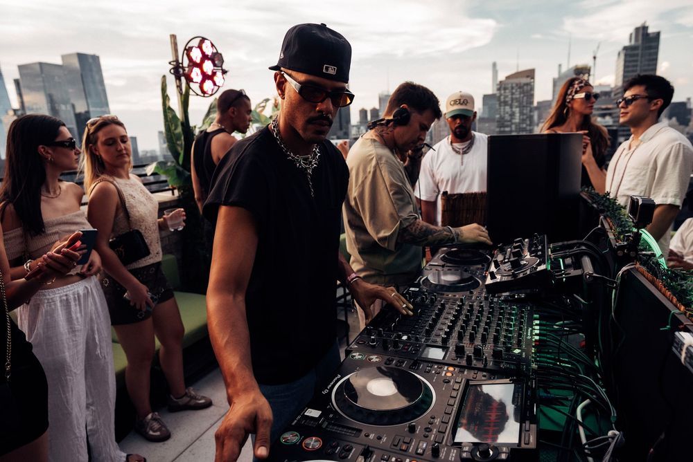People gather around DJ equipment on an outdoor rooftop venue during a party or event.