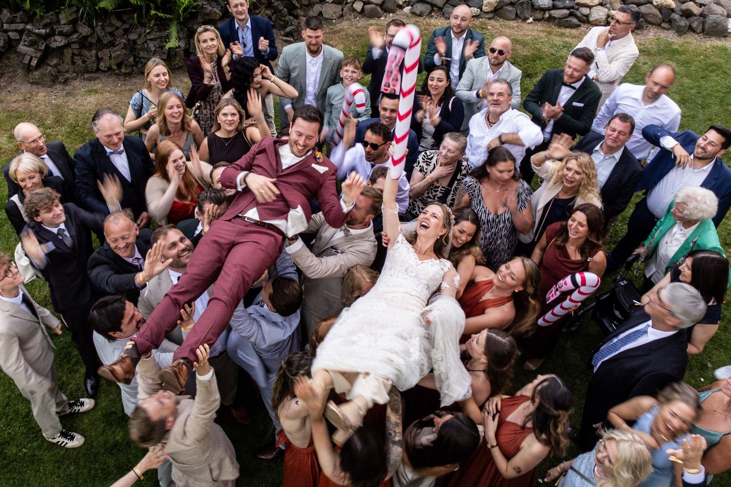 Hochzeitsfotograf Kleve: Authentisches Gruppenfoto mit Brautpaar in Hochstimmung, getragen von Gästen bei ausgelassener Feier im Freien.