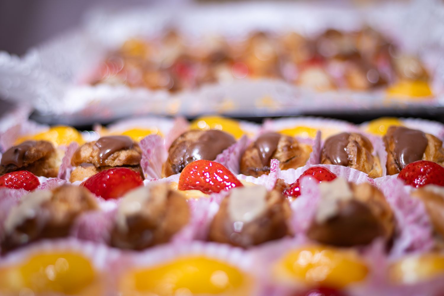Close-up of colorful pastries topped with fresh raspberries, chocolate drizzle, and citrus garnishes on display.